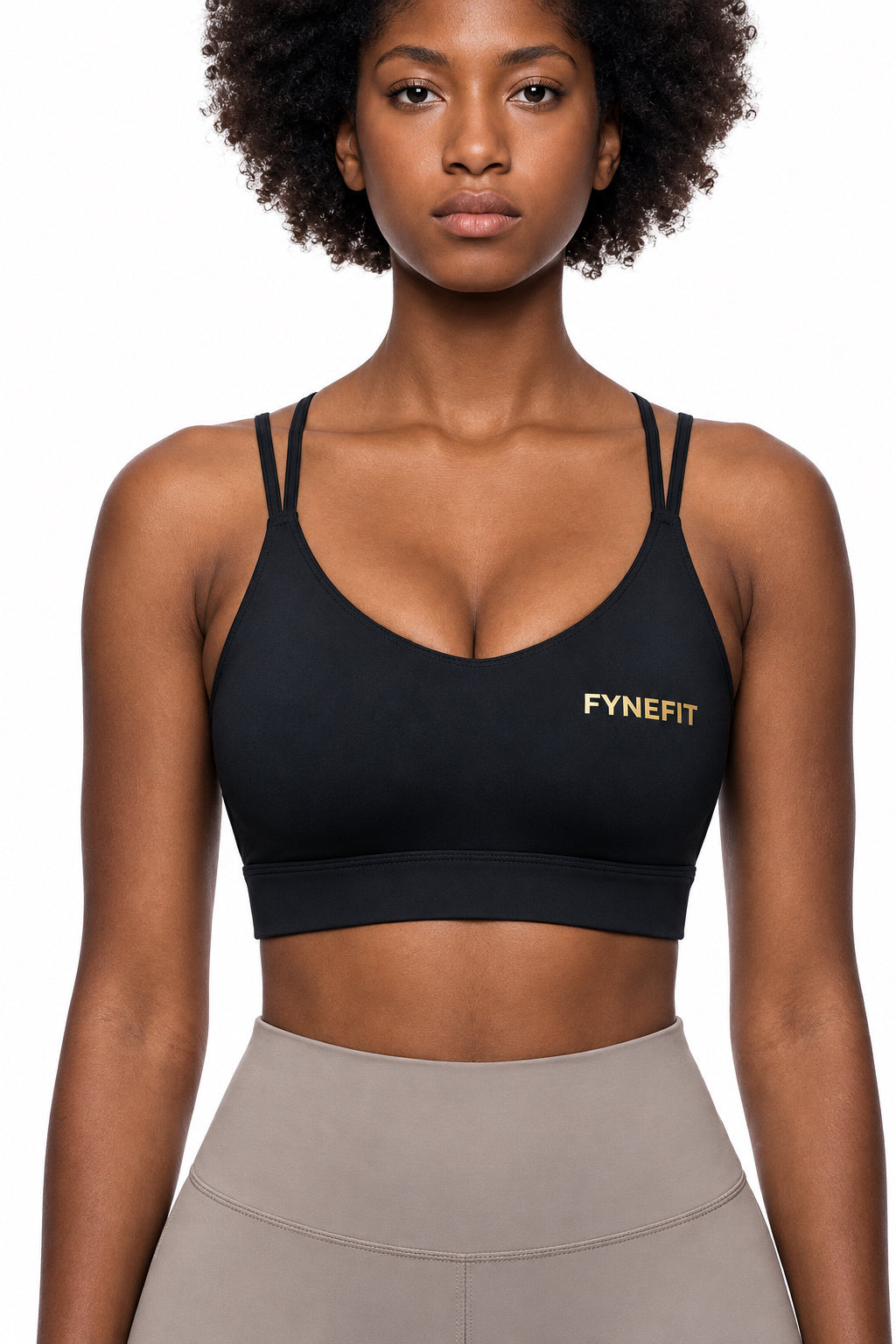 A woman wearing a black sports bra with gold 'FYNEFIT' branding on the left chest
