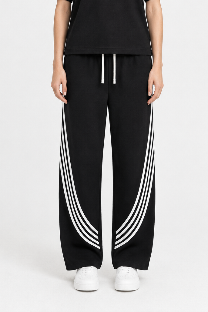 Model wearing ODMPOD FF Varsity Club curved stripe straight sweatpants with white trainers, showcasing relaxed-fit athletic loungewear.